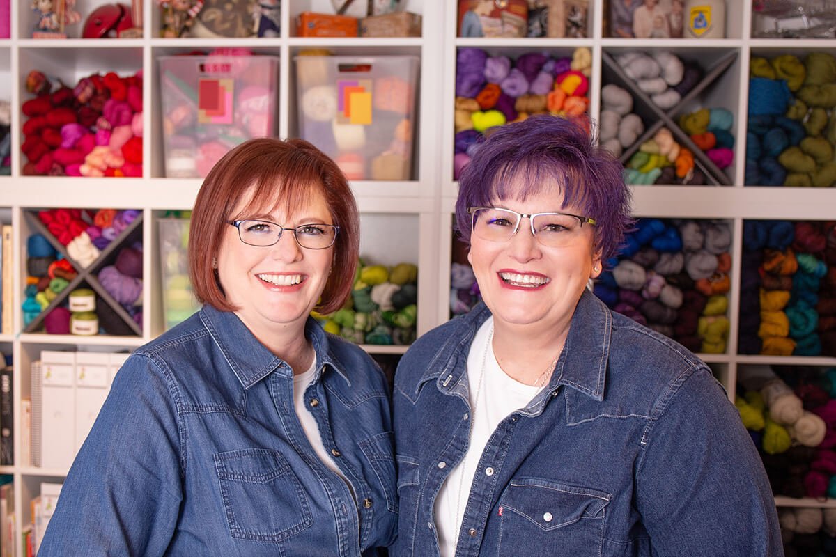 Two professional organizers standing in front of a large wall of yarn smiling for a headshot.